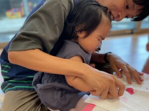 職員の先生が園児と一緒に絵の具のスタンプをギュッと強く押している様子